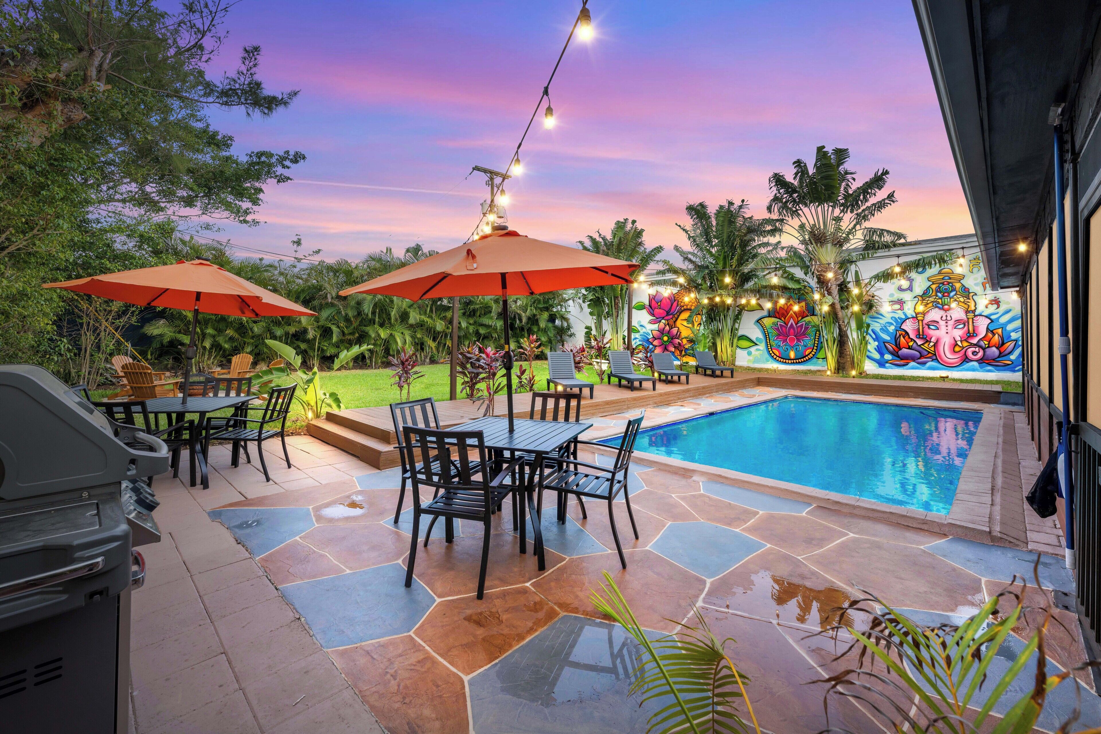 An outdoor pool area with a barbecue grill, tables, and umbrellas.