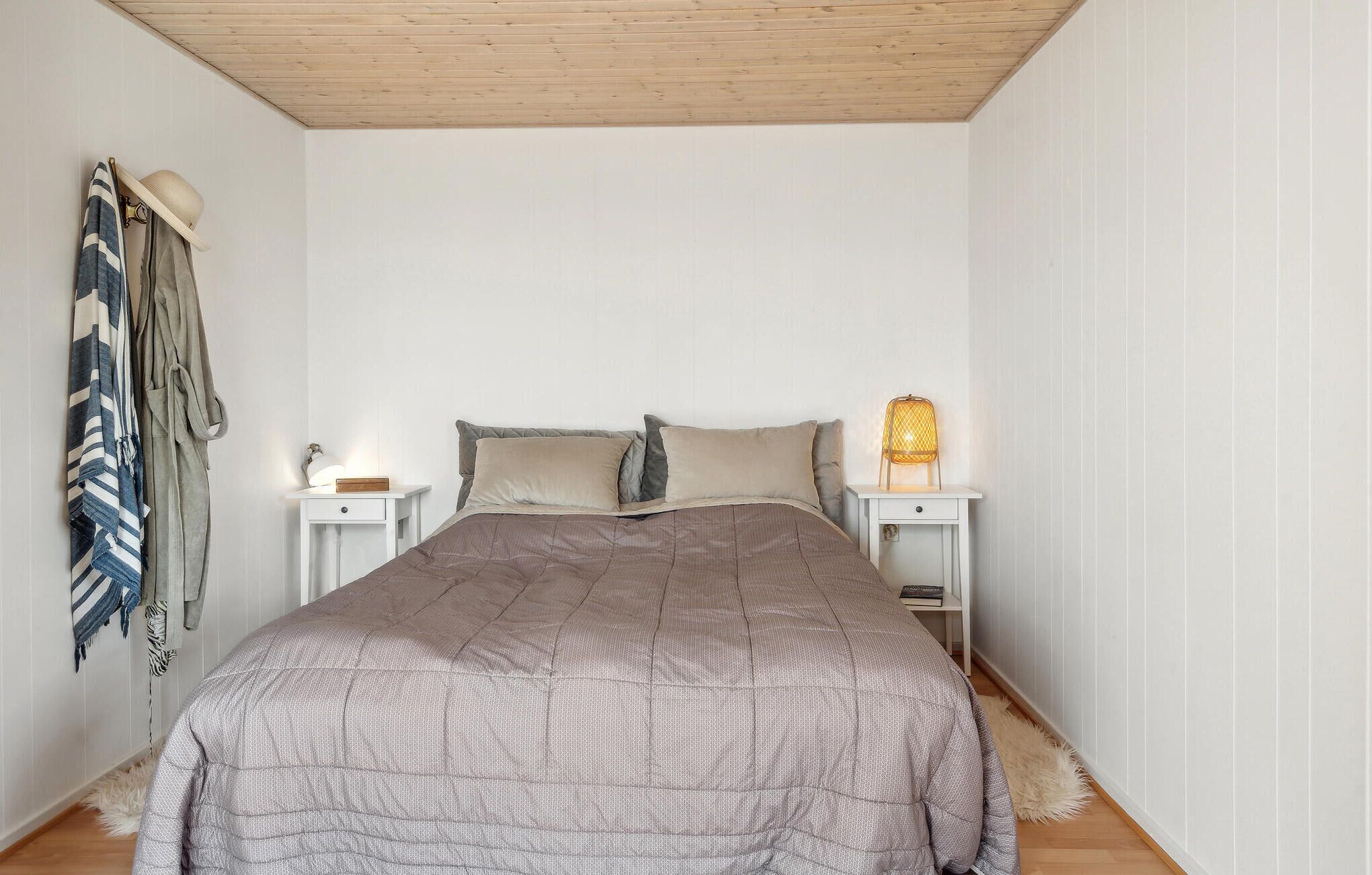 Een slaapkamer met een bed, twee nachtkastjes, een lamp en een hoed aan de muur.