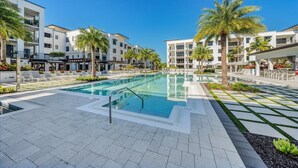 A modern hotel with a central swimming pool, surrounded by palm trees and lounge chairs.
