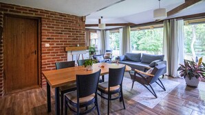 Ein Essbereich mit Backsteinwand, Holztisch und Stühlen. Im Hintergrund befindet sich eine Couch und ein Fenster mit Vorhängen.