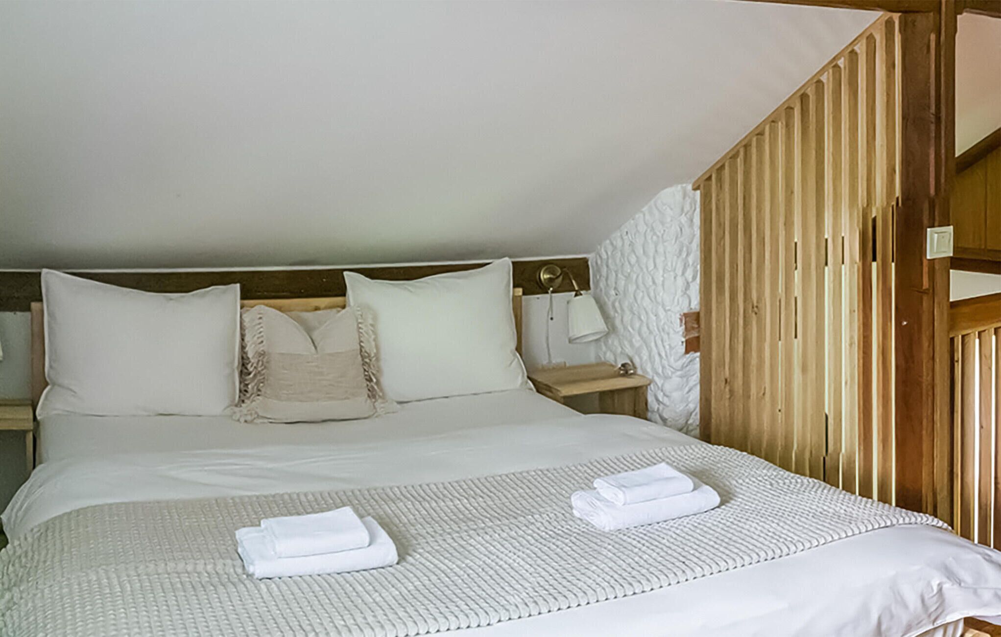 A neatly made bed with white linens and pillows, a bedside table with a lamp, and a wooden slat wall.