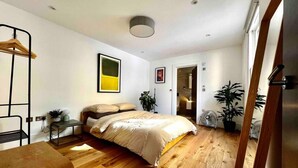 A bedroom with a bed, bedside table, and a hanging chair. There is a door leading to a bathroom.