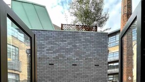 A modern patio with a brick wall, tiled flooring, and potted plants.