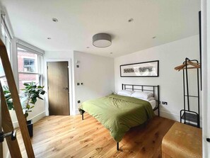 A bedroom with a bed, a wooden floor, a window, and a door. - Modern Retreat in the Heart of Shoreditch (London)