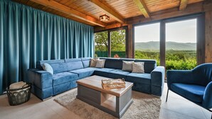 A modern living room with a sectional sofa, a coffee table, and a view of a green landscape through large windows. - Nice home in Stubicke Toplice with sauna (Stubicke Toplice)