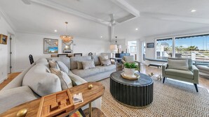 Uma sala de estar ampla com um sofá grande, uma mesa de centro e vista para o exterior.