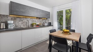 A modern kitchen with a built-in oven, a coffee maker, and a microwave. There is a dining table with chairs and a bowl of fruit. - Lovely home in Kraljevica with house sea view (Kraljevica)