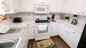 Cocina compacta con armarios blancos, microondas, estufa, fregadero y cafetera.