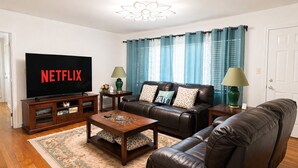 Sala de estar con televisor, sofás de cuero, una mesita de centro y alfombra estampada.