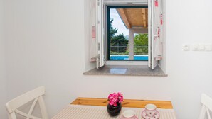 A room with a wooden table, a vase with pink flowers, a teacup and saucer, and a window with a view of a swimming pool and greenery. - Gorgeous home in Bajagic (Bajagic)