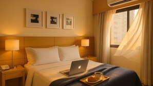 A hotel room with a bed, two bedside lamps, a laptop, a tray with a croissant and a cup, and three framed pictures on the wall. - Elegance Suites Congonhas (São Paulo)