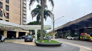 A modern building with a covered entrance, palm trees, and a multi-level parking structure. - Elegance Suites Congonhas (São Paulo)