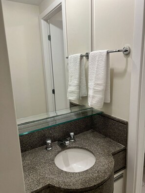 A bathroom with a granite countertop, a white sink, and a glass shower enclosure.