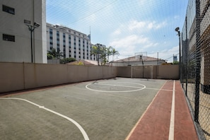 An indoor basketball court with a netted enclosure, surrounded by a building with multiple windows and a red-tiled roof.