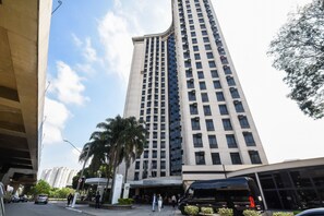 A tall hotel with a modern design, featuring a prominent entrance and a large parking area.