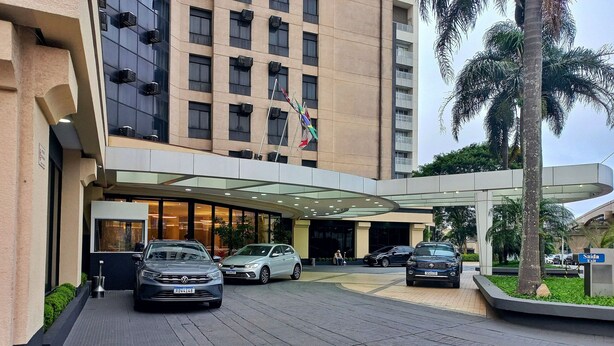 A hotel entrance with a covered walkway, multiple cars parked, and a palm tree. - Elegance Suites Congonhas (São Paulo)