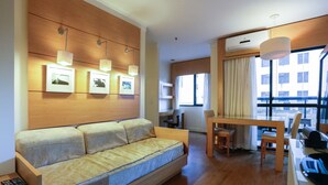 A modern hotel room with a sofa, a dining table, chairs, a desk with a computer, and a large window with curtains. - Elegance Suites Congonhas (São Paulo)