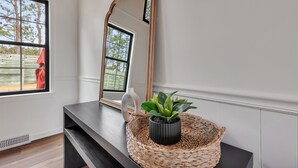 A room with a large mirror, a potted plant, and a woven basket on a dark console table. - Charming ranch in Wilmington (Wilmington)