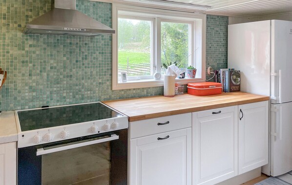 A kitchen with a stove, oven, white cabinets, a window with a view of greenery, and a white refrigerator.