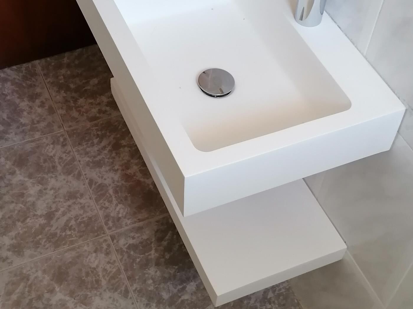 A white bathroom sink with a single drain, a white countertop, and a tiled floor.