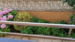 A balcony with a decorative railing, a stone wall, and a variety of plants including hydrangeas and yellow flowers. - Apartment 4/6 ground floor terrace (L'Estartit)