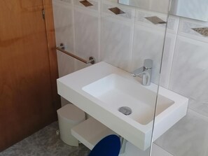 Une salle de bain avec un lavabo blanc, des toilettes et une petite poubelle.