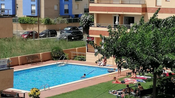 A rectangular swimming pool with a diving board, surrounded by a grassy area and a few trees. - Apartment 4/6 ground floor terrace (L'Estartit)
