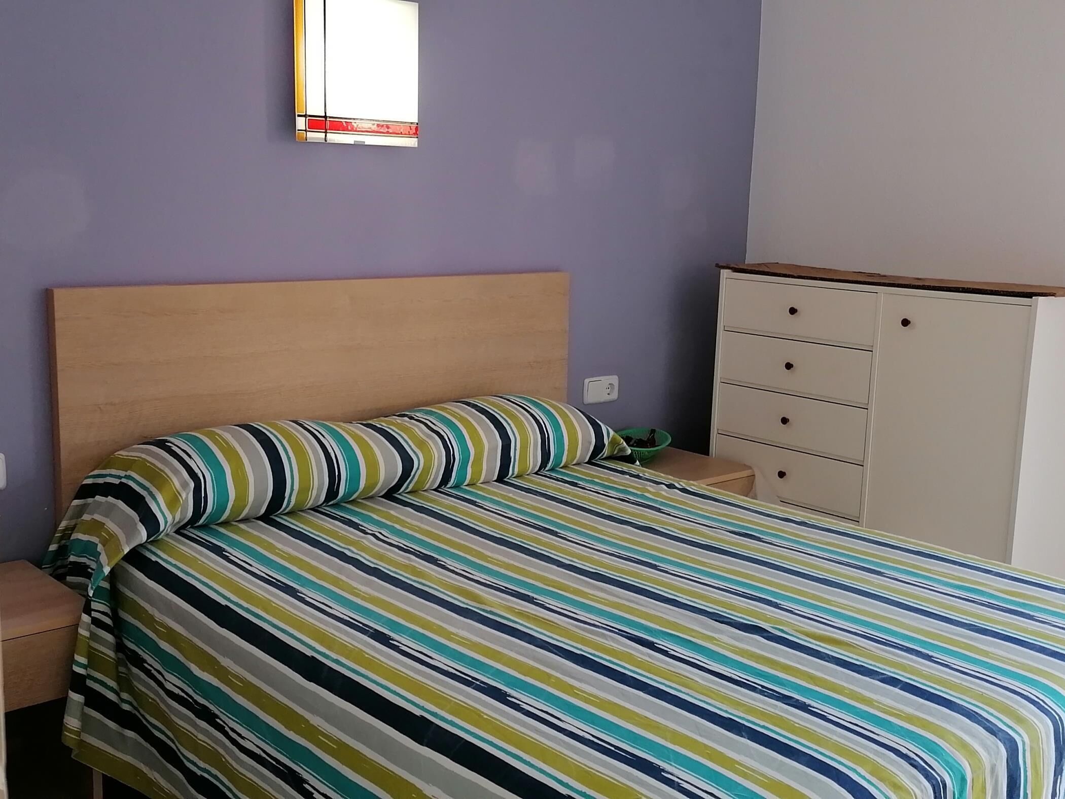 Une chambre à coucher avec un lit, une table de chevet, une commode et un miroir au mur.