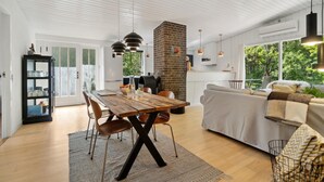 Een ruime woonkamer met een houten eettafel, een bank en een keuken met een schouw van baksteen.