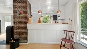 Een moderne keuken met een bakstenen muur, hanglampen, een houten stoel en uitzicht op groen.
