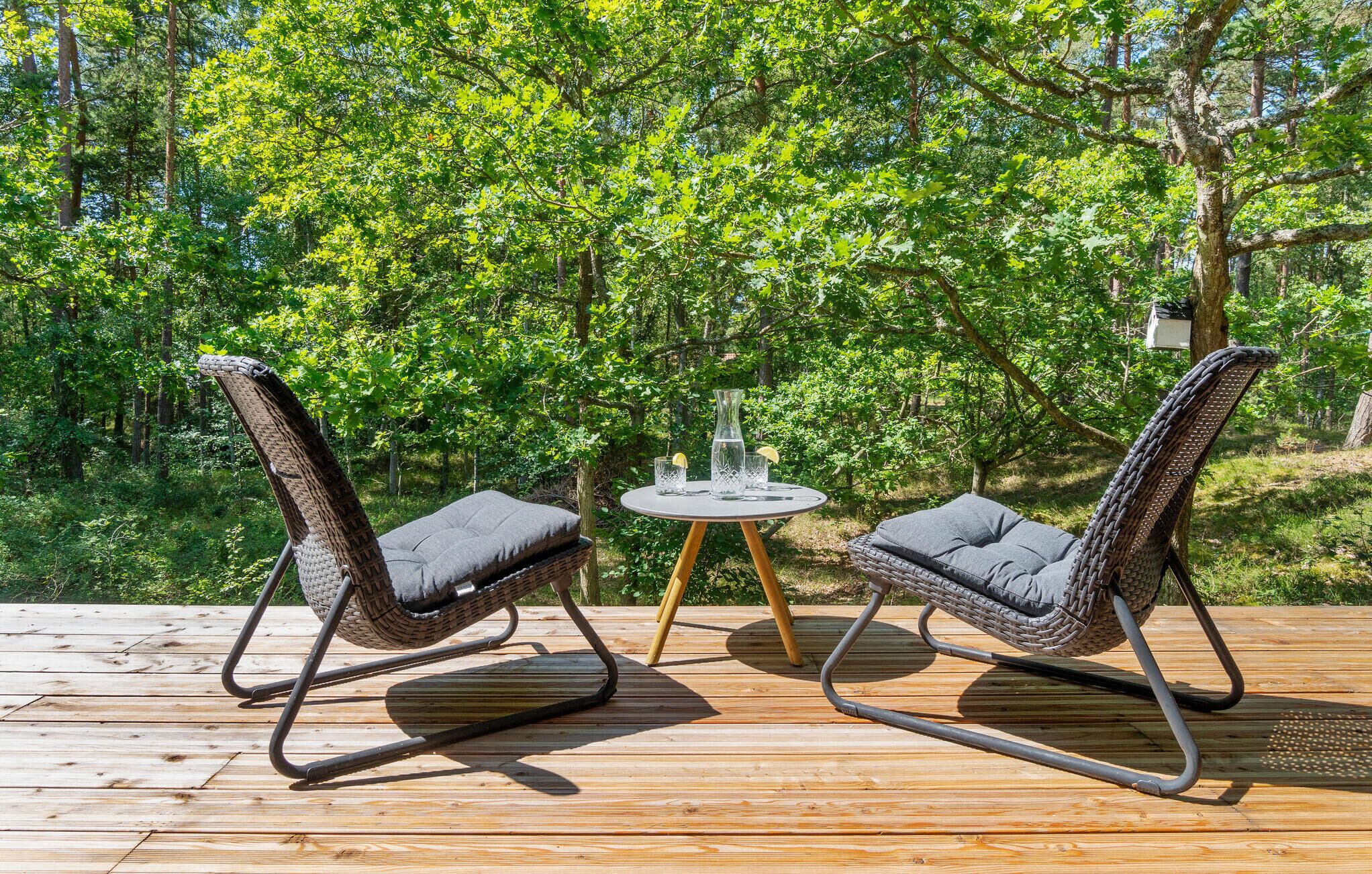 Une terrasse en bois avec deux fauteuils en osier et une petite table ronde sur laquelle sont posées des boissons.