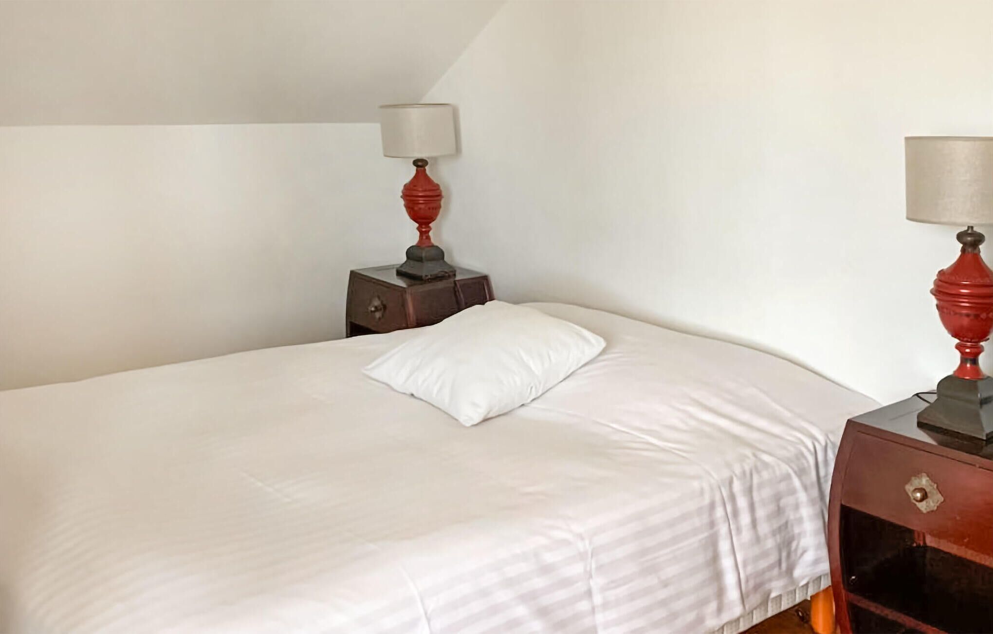 A neatly made bed with a white pillow and a wooden nightstand with a lamp.