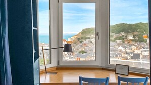 A room with a bay window overlooking a coastal town, a desk with chairs, and a lamp. - Beautiful home in étretat with WiFi (Étretat)