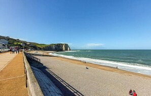 A coastal promenade with a pebble beach, a sea arch, and a promenade with people walking. - Beautiful home in étretat with WiFi (Étretat)