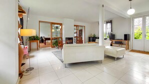 A spacious living room with a white sofa, a television, and a dining area with a table and chairs. - Beautiful home in étretat with WiFi (Étretat)