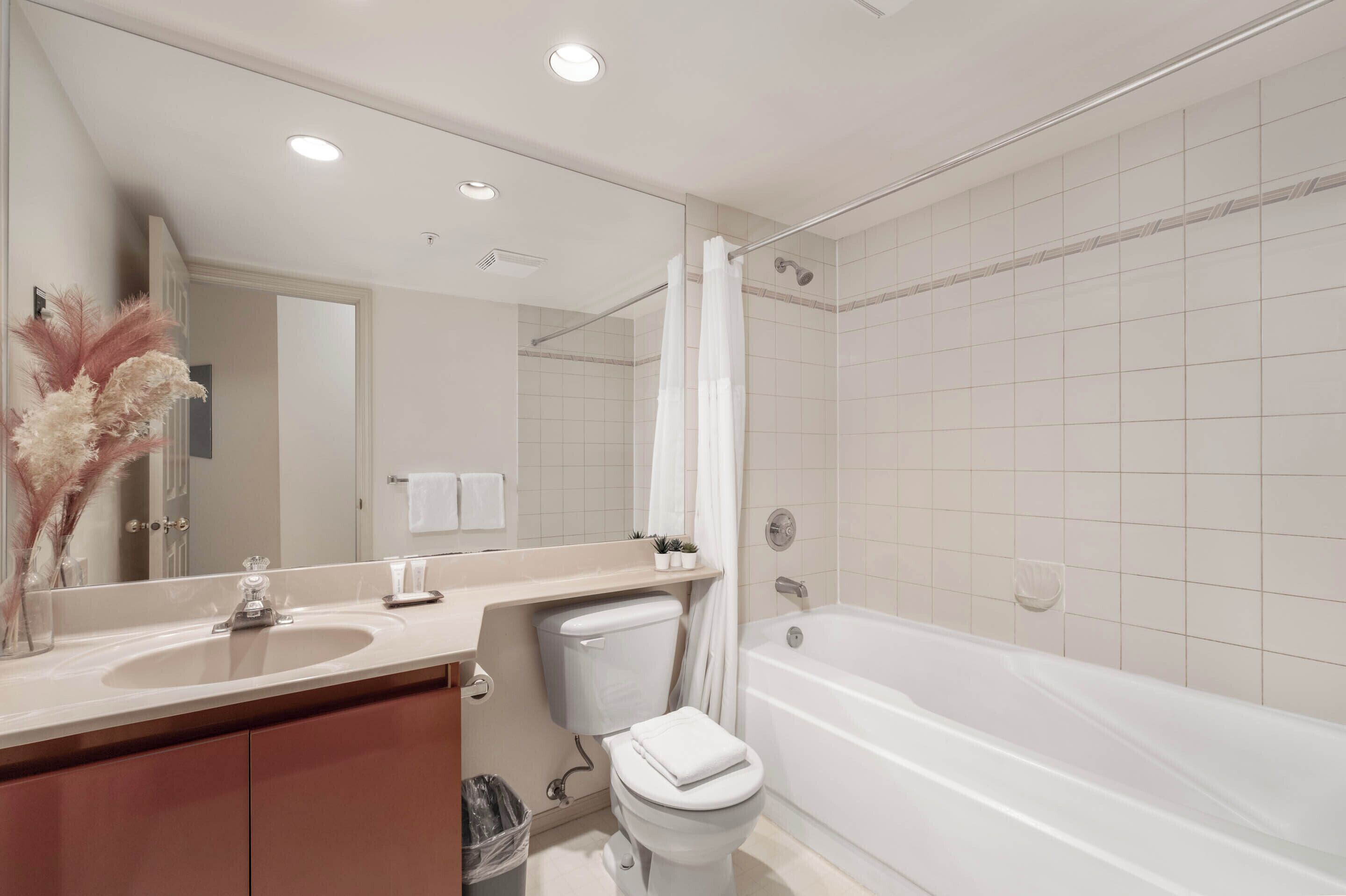 A modern bathroom with a large mirror, a sink, a toilet, and a bathtub.
