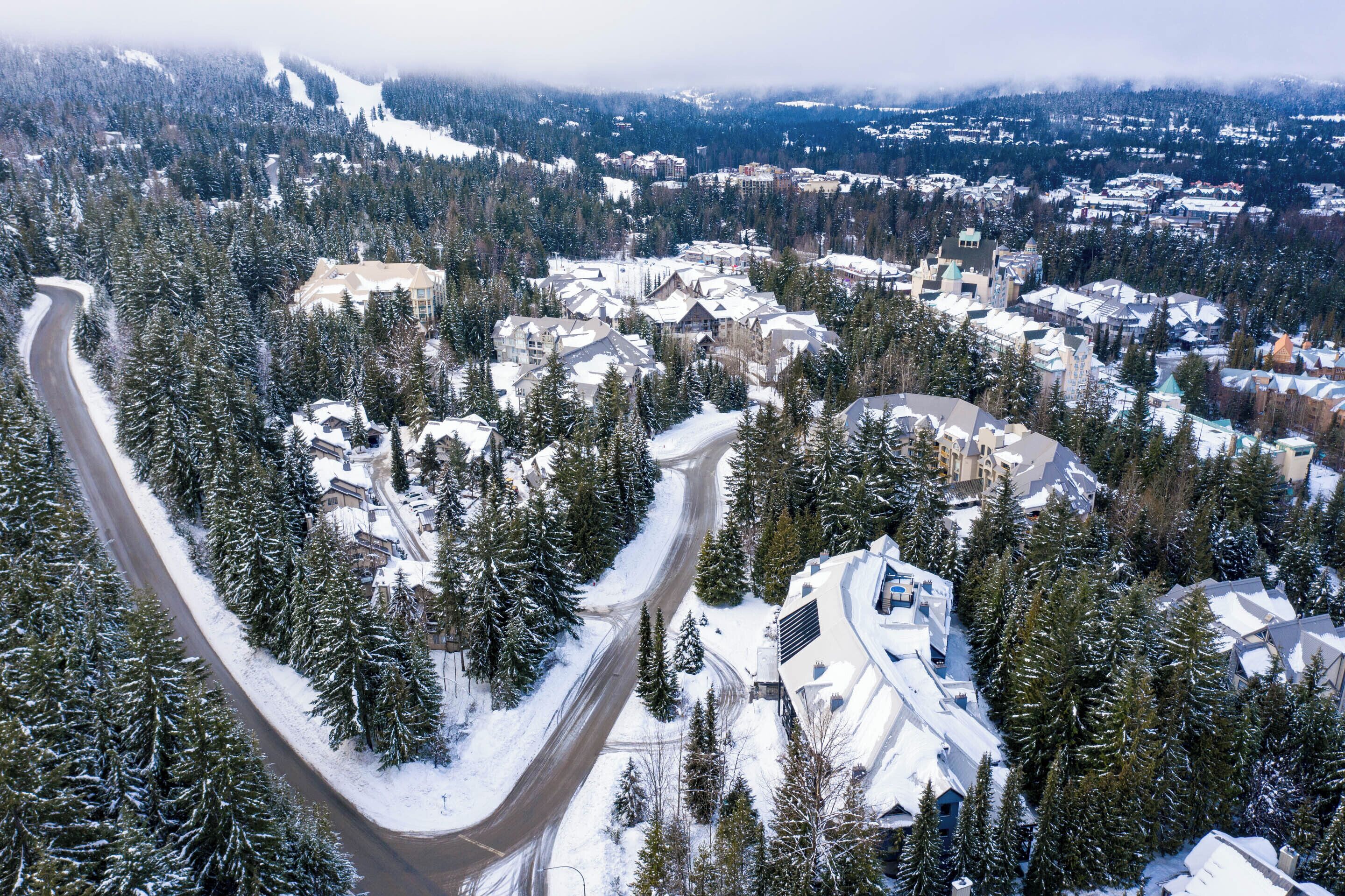 A snow-covered mountain town with a winding road and dense forest.