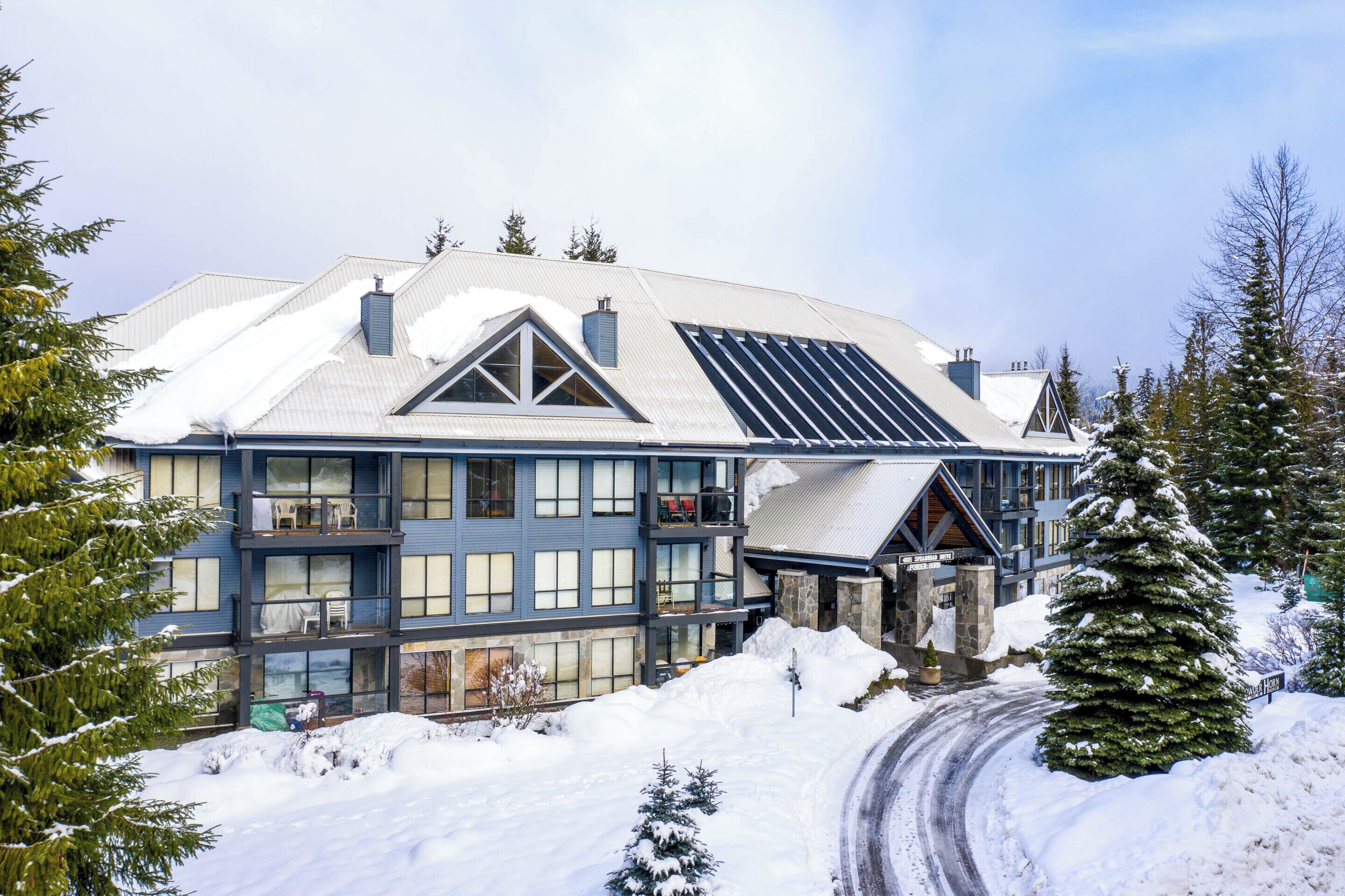 A large, multi-story building with a snow-covered roof, large windows, and a ski lift visible in the background.