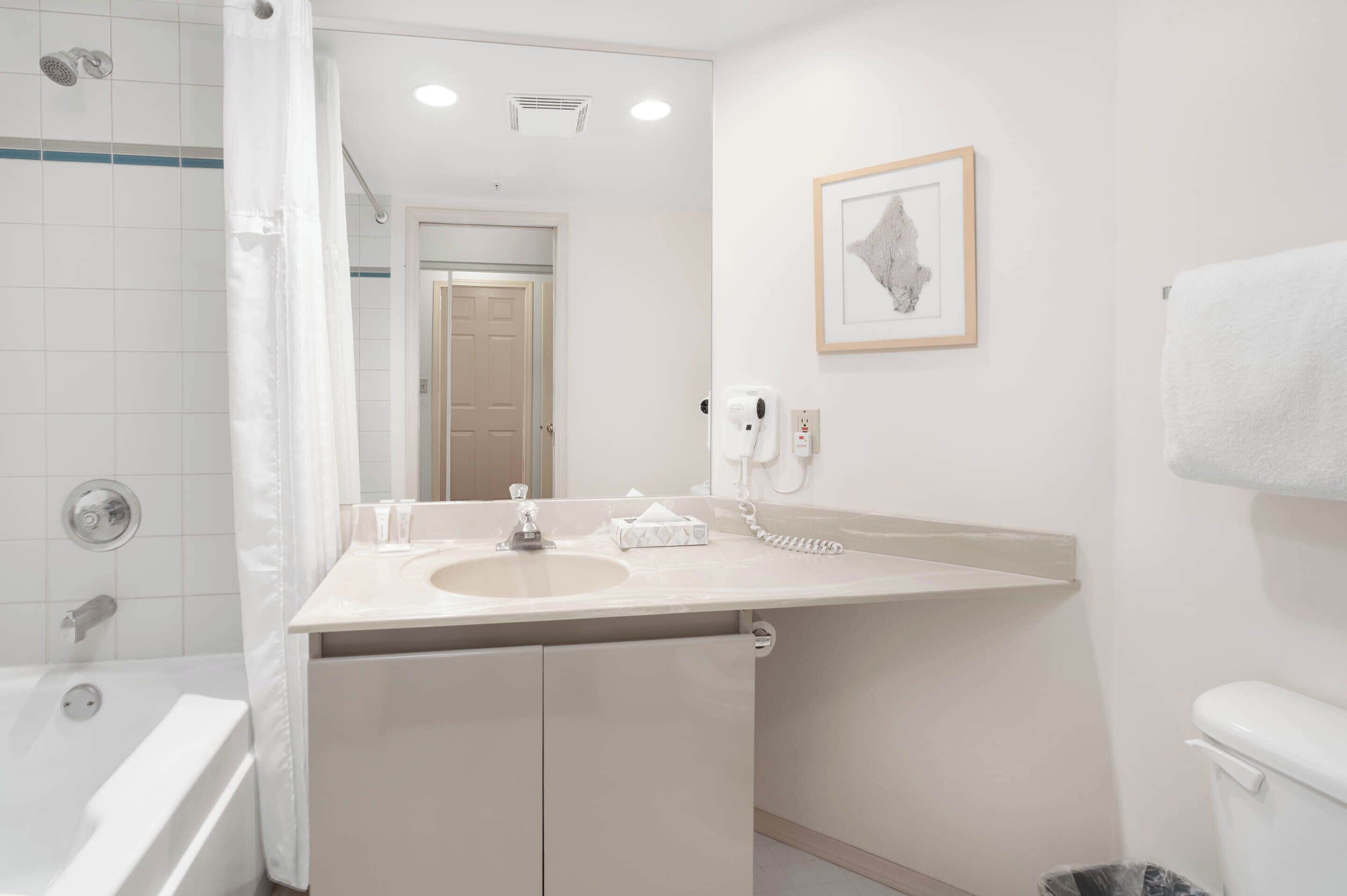 Een moderne badkamer met een bad, een wastafel met een meubel eronder, een fotoraam aan de muur en een telefoon.