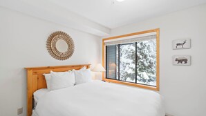 A bedroom with a wooden headboard, a large bed, a window with a view of snow-covered trees, and two wall-mounted animal pictures. - Powderhorn by Whistler Premier (Whistler)