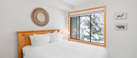 Un dormitorio con cabecera de madera, una cama grande, una ventana con vistas a árboles cubiertos de nieve y dos cuadros de animales colgados en la pared.