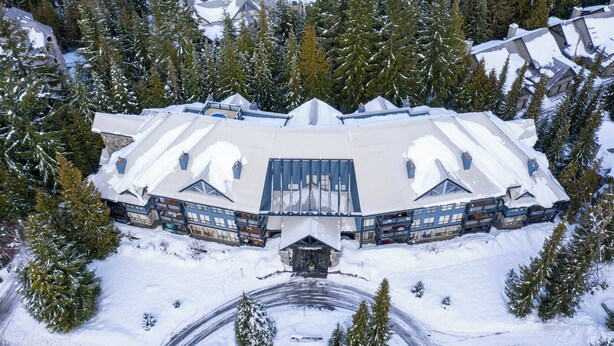 A large, multi-story lodge with a symmetrical roof design, surrounded by snow-covered trees. - Powderhorn by Whistler Premier (Whistler)