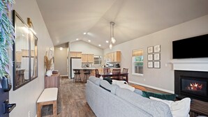 A modern living room with a grey sectional sofa, a fireplace, and a kitchen in the background.