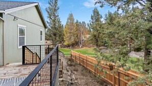 A house with a deck, a fenced yard, and a view of trees.