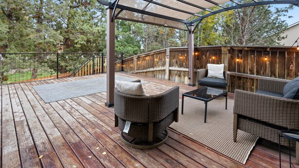 An outdoor deck with wicker furniture, a pergola, and a wooden fence.