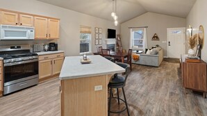 A spacious kitchen with wooden cabinets, a central island, and modern appliances. There is a dining area with a fireplace and a cozy seating arrangement.