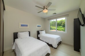 A bedroom with two beds, a ceiling fan, and a window with a view of greenery.