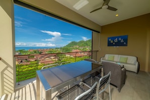 A balcony with a glass table and chairs, a white sofa, and a ceiling fan.
