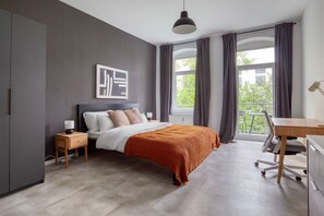 Un dormitorio moderno con una cama grande, una mesita de noche, un escritorio y una ventana con cortinas.