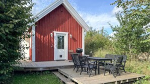 A red wooden building with a white door, a small porch with a table and chairs, and a grill. - 1 bedroom amazing home in Blomstermåla (Blomstermåla)